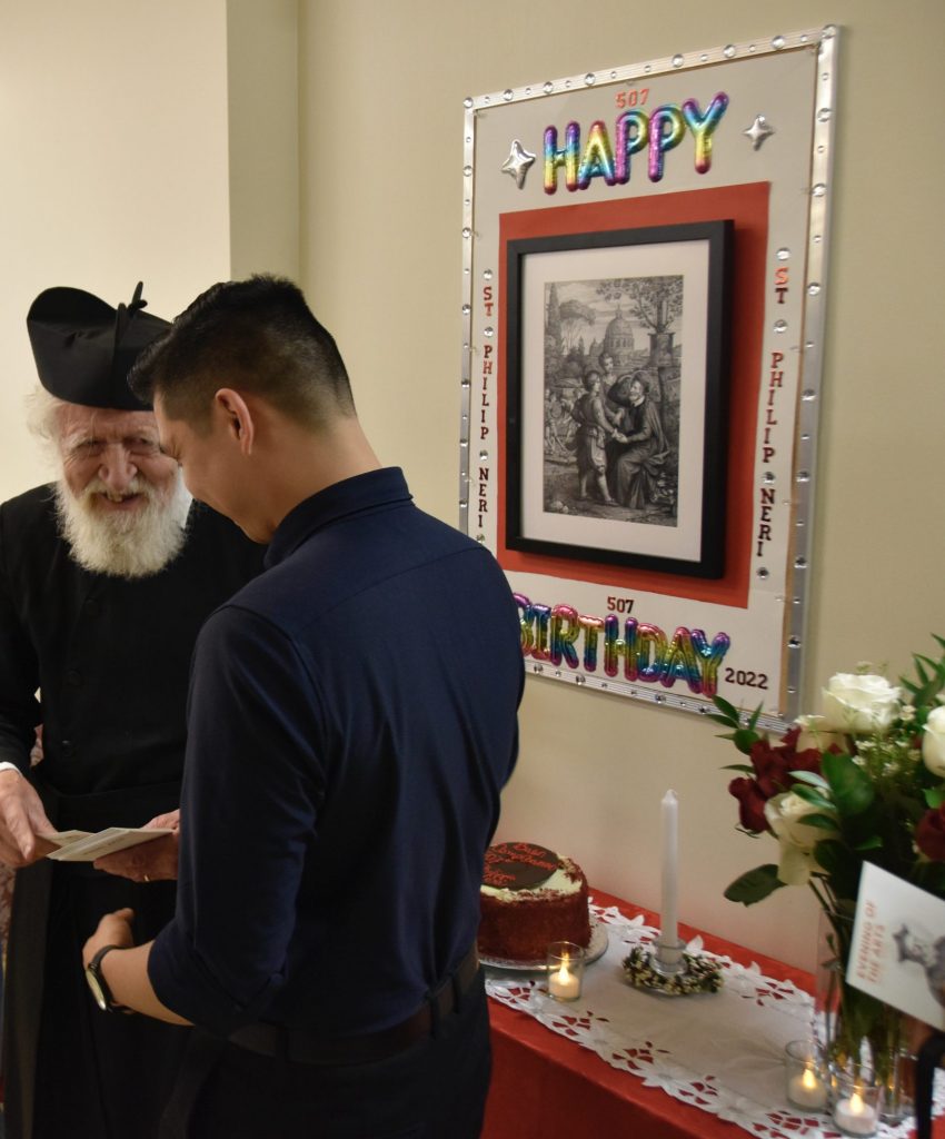 A parishioner dressed as St Philip hands out programs in front of the Happy Birthday sign