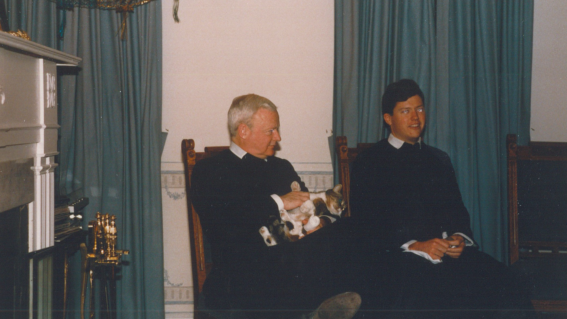 Fr Robinson petting the house cat next to Fr Daniel
